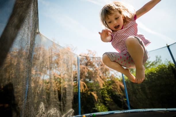 Child jumping high on big trampoline outside in garden